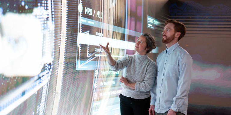 Two people talking while looking at a big screen.